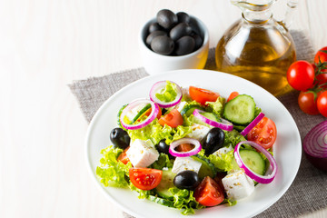 Fresh Greek salad made of cherry tomato, ruccola, arugula, feta, olives, cucumbers, onion and spices. Caesar salad in a white bowl on wooden background. Healthy organic diet food concept.