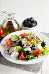 Fresh Greek salad made of cherry tomato, ruccola, arugula, feta, olives, cucumbers, onion and spices. Caesar salad in a white bowl on wooden background. Healthy organic diet food concept.