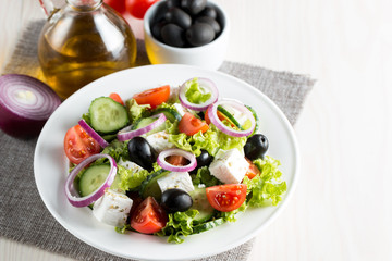 Fresh Greek salad made of cherry tomato, ruccola, arugula, feta, olives, cucumbers, onion and spices. Caesar salad in a white bowl on wooden background. Healthy organic diet food concept.