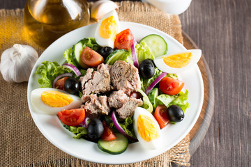 Fresh fish tuna salad made of tomato, ruccola, tuna, eggs, arugula, crackers and spices. Caesar salad in a white bowl on wooden background