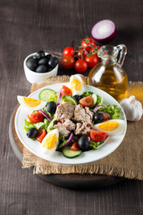 Fresh fish tuna salad made of tomato, ruccola, tuna, eggs, arugula, crackers and spices. Caesar salad in a white bowl on wooden background