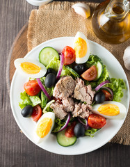 Fresh fish tuna salad made of tomato, ruccola, tuna, eggs, arugula, crackers and spices. Caesar salad in a white bowl on wooden background