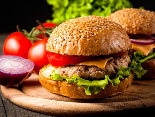 Close-up photo of home made hamburger with beer made of beef, onion, tomato, lettuce, cheese and spices. Fresh burger closeup on wooden rustic table with potato fries and chips.