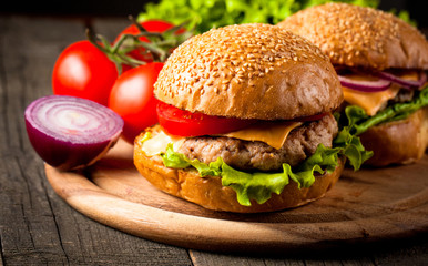 Close-up photo of home made hamburger with beer made of beef, onion, tomato, lettuce, cheese and spices. Fresh burger closeup on wooden rustic table with potato fries and chips.