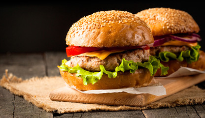 Close-up photo of home made hamburger with beer made of beef, onion, tomato, lettuce, cheese and spices. Fresh burger closeup on wooden rustic table with potato fries and chips.
