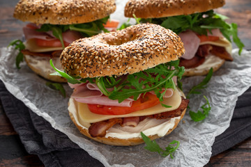 Fresh Bagels Sandwiches with cream cheese, bacon, tomato and green wild rocket on rustic wooden...