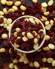 Healthy snack of Dried cranberries and macadamia nuts in a ceramic bowl on rustic wooden table