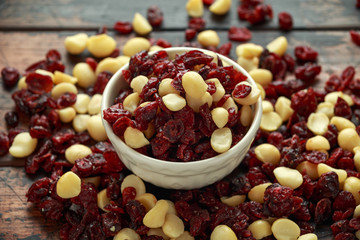 Healthy snack of Dried cranberries and macadamia nuts in a ceramic bowl on rustic wooden table