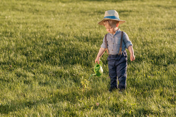 Naklejka na ściany i meble Toddler child outdoors. One year old baby boy wearing straw hat using watering can