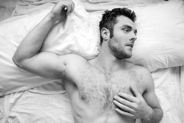 Shirtless sexy hunky man with beard and six pack abs lies naked in bed