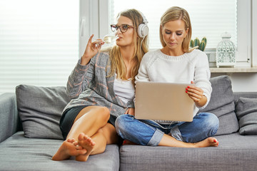 Obraz premium two young women and women sit on a gray couch with a computer and listen to music