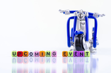 UPCOMING EVENT word block and miniature motorcycle concept on white reflection table
