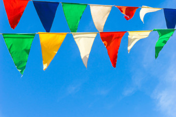 Multicolored flags a triangular shape  against the blue sky. Good background on the theme of a city street holiday
