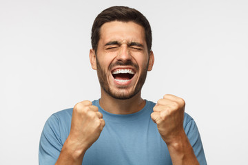 Closeup of emotional man isolated on gray background, screaming with joy and victorious expression,...