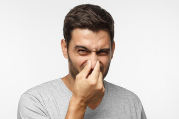 Close up portrait of young man holding his nose as if smelling something rotten and stinky, trying to find source of odor