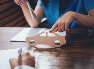 Man signing a car insurance policy, the agent is holding the wooden car model.