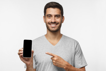 Young smiling man holding blank phone with empty black screen, isolated on gray background
