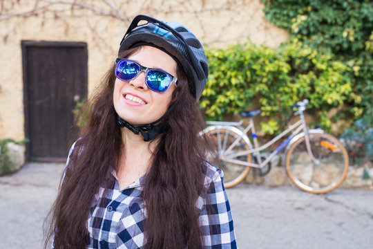 Happy woman with helmet and sunglasses posing backgound bicycle and street