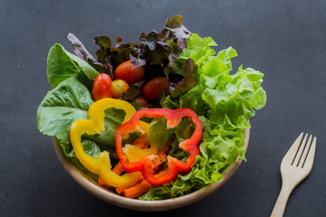 Bowl of fresh vegetable salad with wooden fork on black background.Clean eating, dieting, vegan food concept.