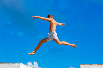 young man doing parkour jump on the blue sky background on sunny summer day