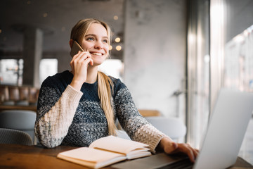 Young cheerful  woman with emotional face speaks on mobile phone and smiling in loft office....