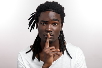 Black man says shh, keeps fingers on lips, asks not tell secret on white background