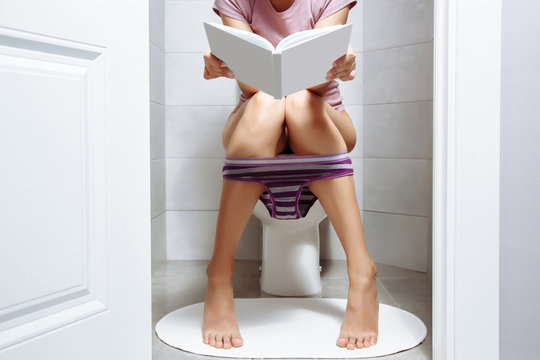 Woman sitting on toilet bowl while reading book - health problem concept