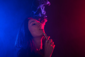 Obraz premium Portrait of young woman in neon red and blue smoke with vape or e-cigarettes