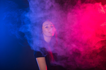 Portrait of young woman in neon red and blue smoke with vape or e-cigarettes