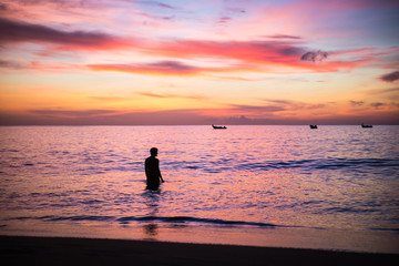 Naklejka na ściany i meble Young man enjoying a purple sky sunset in a calm sea in Caribe, Trinidad and Tobago, Caribe