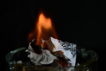 A piece of paper burning in a glass ashtray close up