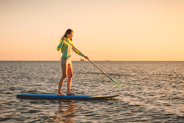 Sporty woman floating at stand up paddle board with colorful sunset colors