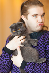 Young man holding a gray Scottish fold cat.