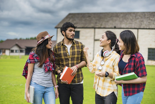 education, school and people concept - Cheerful university students with laptop and read a books on group of students in background at each other at school; Asia studen study.
