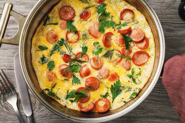 Scrambled eggs with sausage and greens in a frying pan, top view