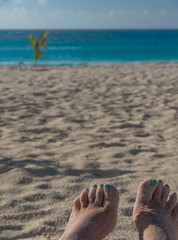 Fototapeta na wymiar View from a beach chair: Sandy bare feet with aqua nail polish the same color as the Caribbean sea across the beach in the Cancun Hotel Zone
