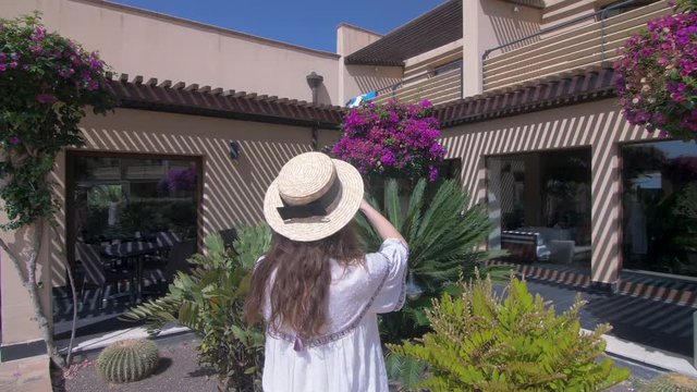 Beautiful woman making mobile photo of nice villa. Young girl taking photo. Dressed in white dress and hat. Female tourist. Slow motion