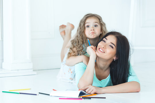 Cute little girl and her mother drawing a picture together indoors.