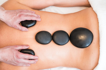 Obraz na płótnie Canvas Masseur massaging woman's back with lava stones