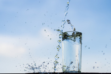 Water dropping into the glass with blue sky background.