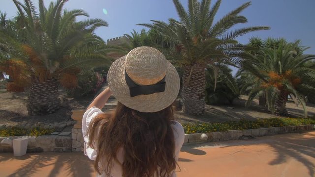 Beautiful woman making mobile photo of nice villa. Young girl taking photo.  Dressed in white dress and hat. Female tourist.Elegant girl have good moments. Slow motion. 