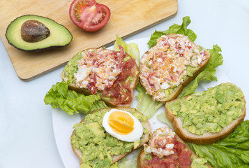 sandwiches with avocados, tomatoes, eggs on leaves of green salad