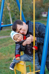 Father rides his son on the swing in the yard and hugs him, it is evident that the son is very pleased that the father spends a lot of time with him. Father's Day