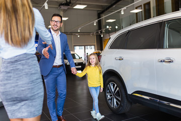 Handsome young man with his cute little daughter choosing a new car at car showroom.