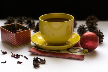 New year and christmas composition of yellow cup of hibiscus tea, Christmas tree cones, tea box and red decorations isolated on white background.