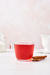 Fruit tea in a glass cup with cinnamon, sugar and milk jug on marble table top with feminine rose background. Copy space.