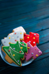 Four homemade glazed gingerbread in form of Christmas tree decorated with stars on plate on wooden table.