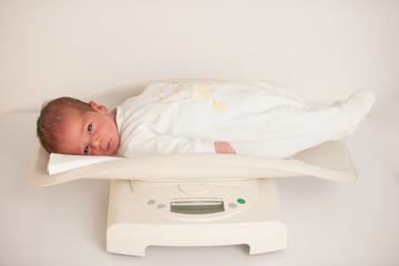 Ten days old new born child on a scale measuring weight