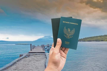 Türaufkleber hand holding Indonesian passport with beach background © yudhistirama