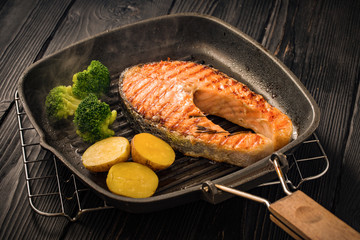 Grilled salmon steak with potatoes and broccoli in old roasted pan